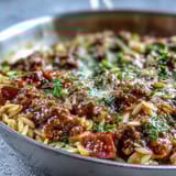 Steam rises from a bowl of the Comforting Ground Beef Orzo Dinner, garnished with fresh parsley and a generous dusting of Parmesan cheese.