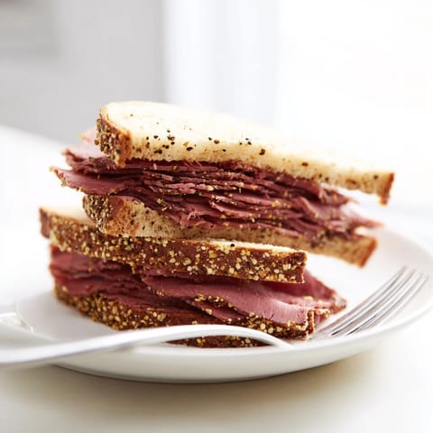Close-up of a loaded pastrami on rye sandwich, layered with savory meat and fresh bread.