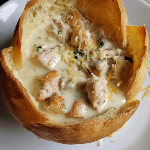 The rich, cheesy Chicken Alfredo filling bubbles inside a toasted crusty bread bowl, garnished with fresh parsley.