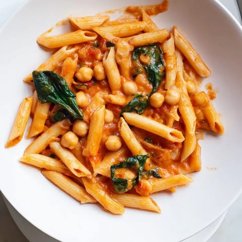 Fork-ready Creamy Tuscan Chickpea Pasta tossed with al dente noodles and fresh basil garnish.