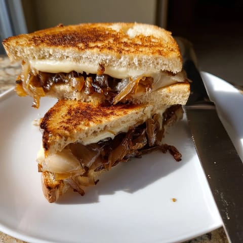 Freshly ground pepper sprinkled over gooey cheese and onions in this Caramelized Onion Grilled Cheese, served beside a steaming bowl of tomato soup.