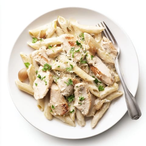 Savory roasted garlic chicken penne garnished with fresh parsley and grated Parmesan, served warm in a white ceramic bowl with steam rising.  