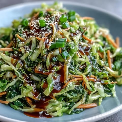 A close-up of Hot and Sour Cabbage stir-fry, featuring crisp green cabbage and orange carrots coated in a glossy, spicy red sauce garnished with scallions.