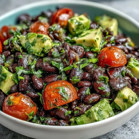 Vibrant black bean and veggie bowl with cherry tomatoes, avocado, and zesty lime dressing, garnished with fresh cilantro.  