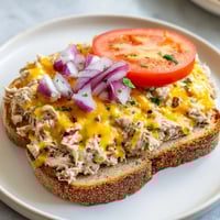 Golden, bubbly tuna melt sandwich, a classic open-faced delight on toasted bread.