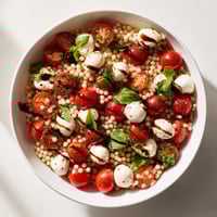A close-up of Caprese Couscous Salad with juicy cherry tomatoes, creamy mozzarella balls, and fresh basil on fluffy pearled couscous.